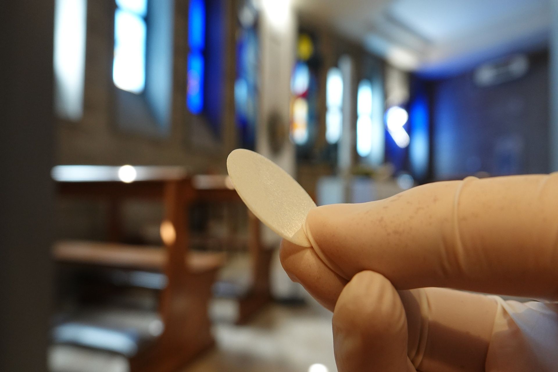 Un'ostia tenuta dalle mani guantate di un sacerdote in tempo di pandemia'
