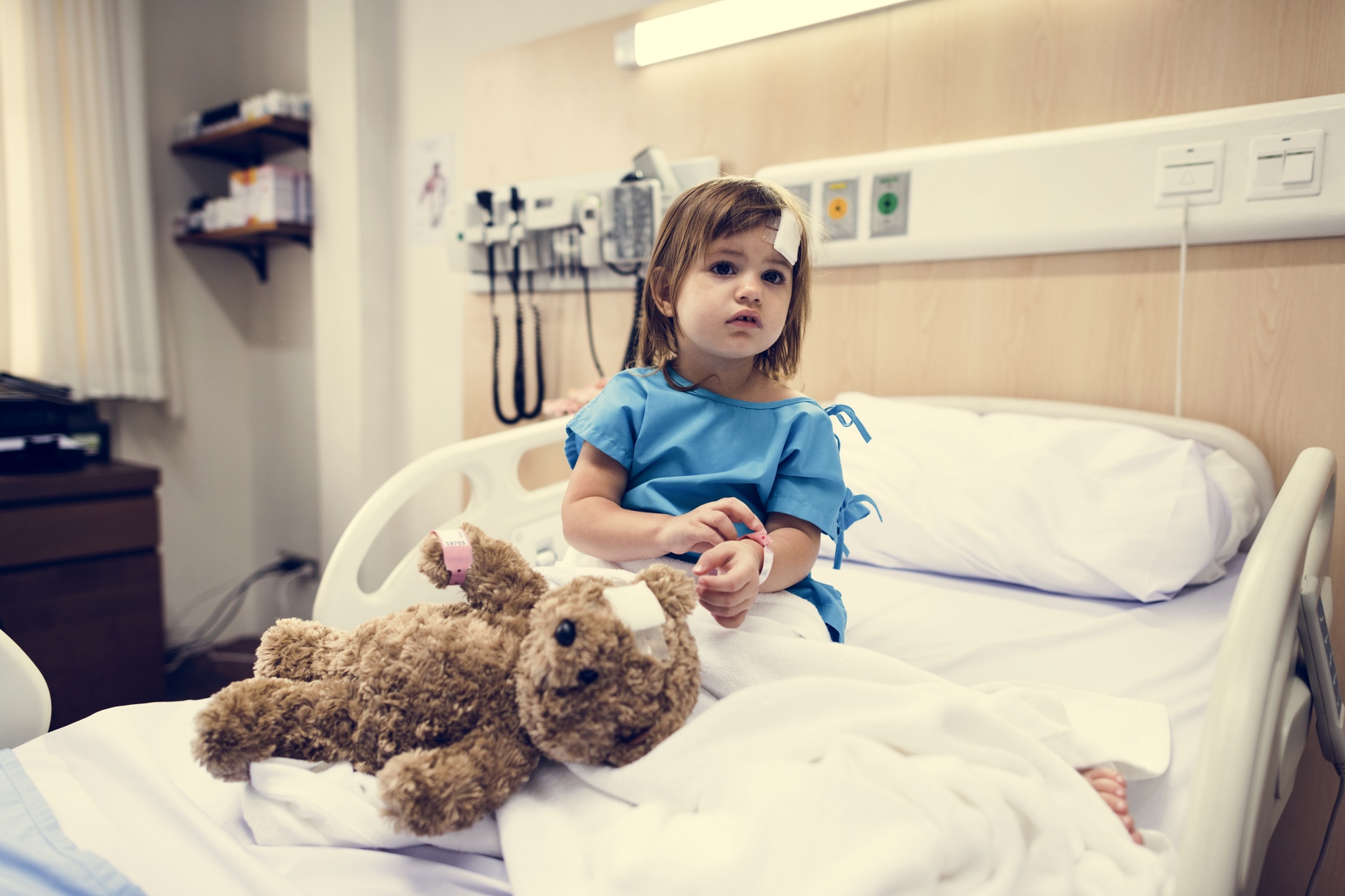 Assistenza sanitaria: una bambina ricoverata in ospedale seduta su un letto accanto al proprio orsacchiotto