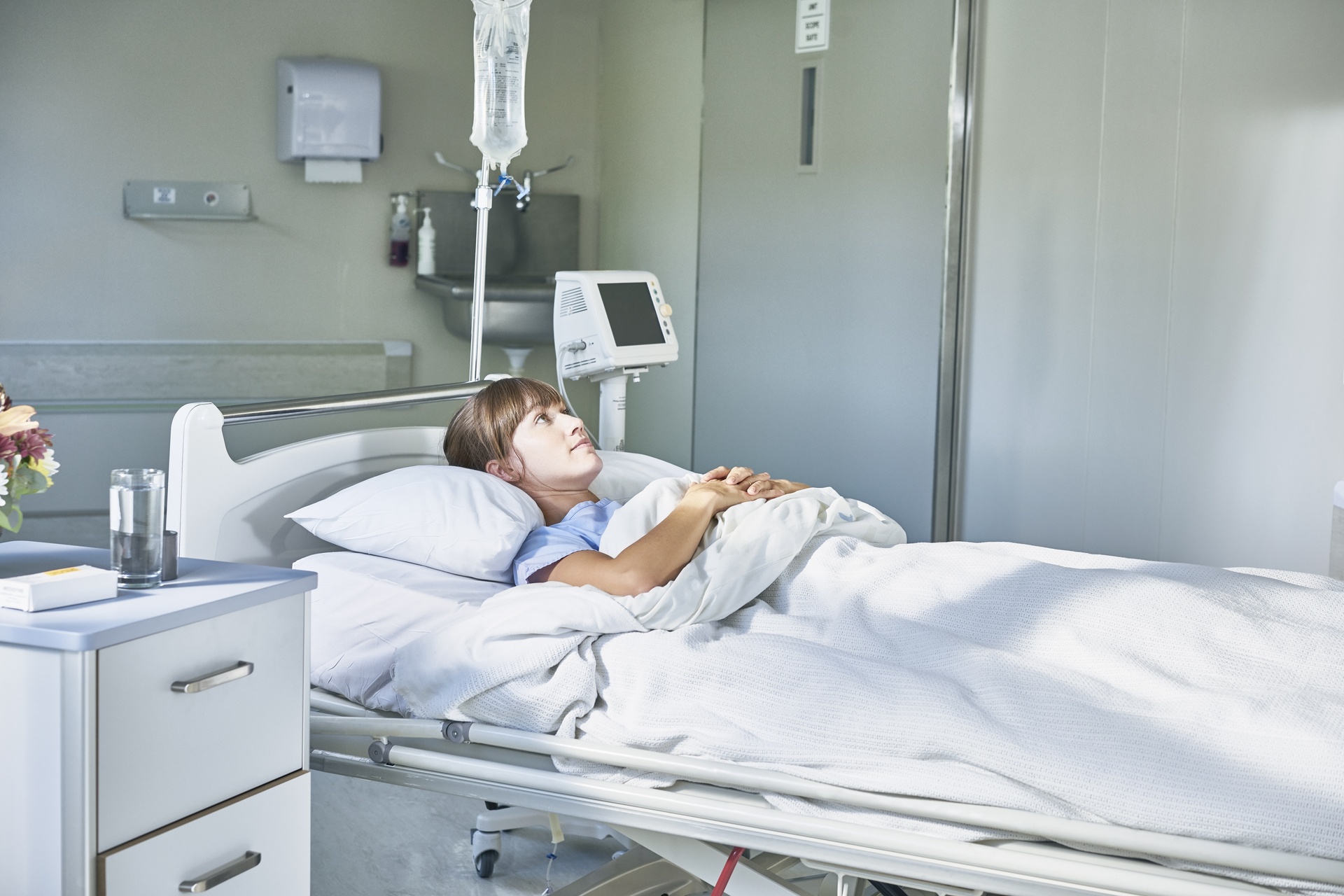 Assistenza sanitaria: un'ammalata giovane ricoverata in un letto d'ospedale e assorta nei propri pensieri