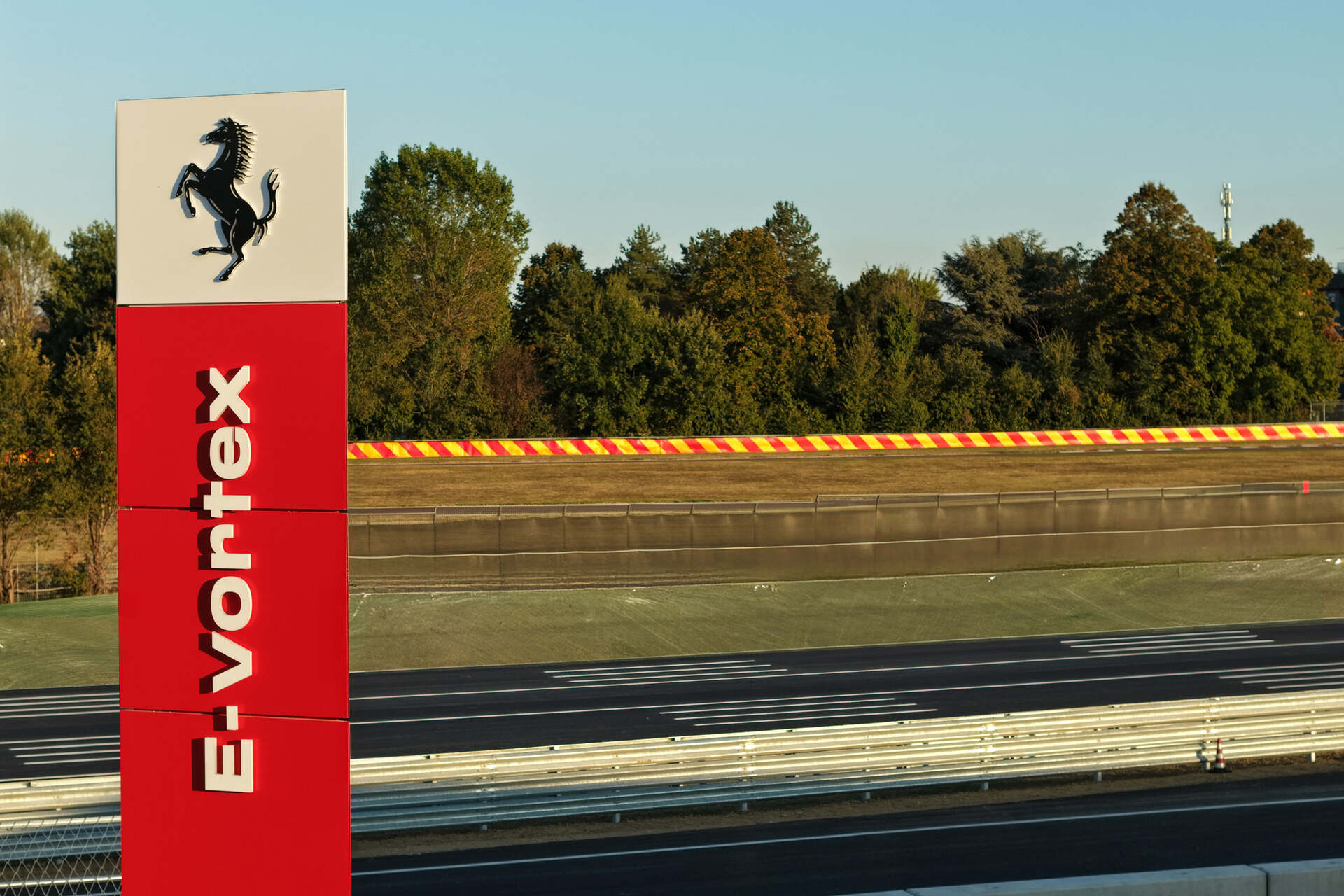 Ferrari e-Vortex: cartello identificativo del nuovo circuito Ferrari sullo sfondo della pista, emblema della tradizione ingegneristica italiana e del futuro dell’innovazione automobilistica