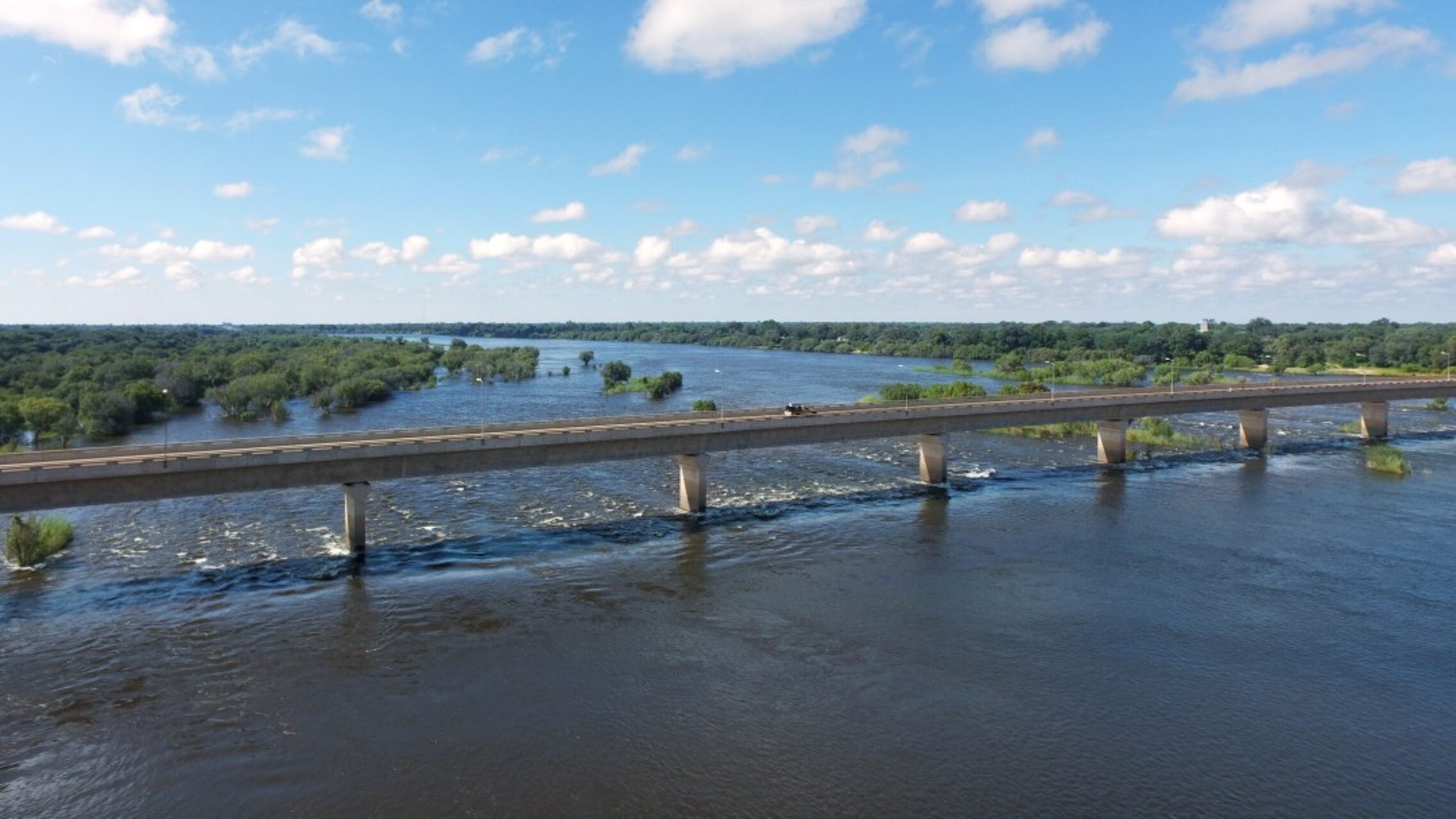 Scorcio generale del fiume Zambesi con il ponte di Katima Mulilo visibile sullo sfondo, punto di passaggio che unisce territori e sostiene traffico, turismo e attività economiche locali