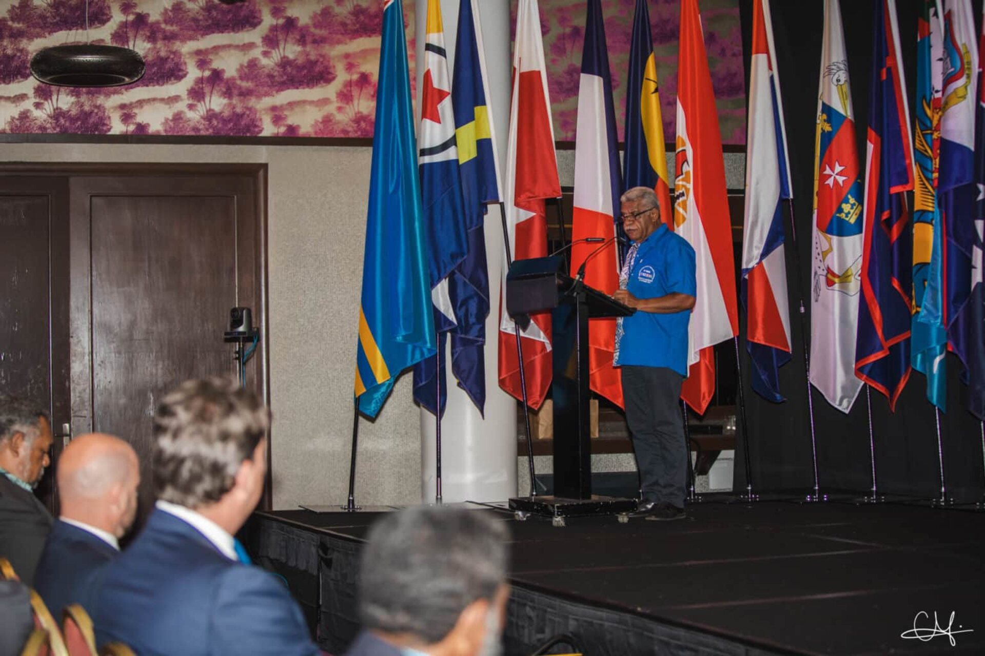 OCTA: intervento del presidente Louis Mapou durante il Forum OCTA, con le bandiere dei territori membri sullo sfondo, a rappresentare cooperazione internazionale, governance condivisa e il ruolo strategico dei territori d’oltremare nello scenario globale