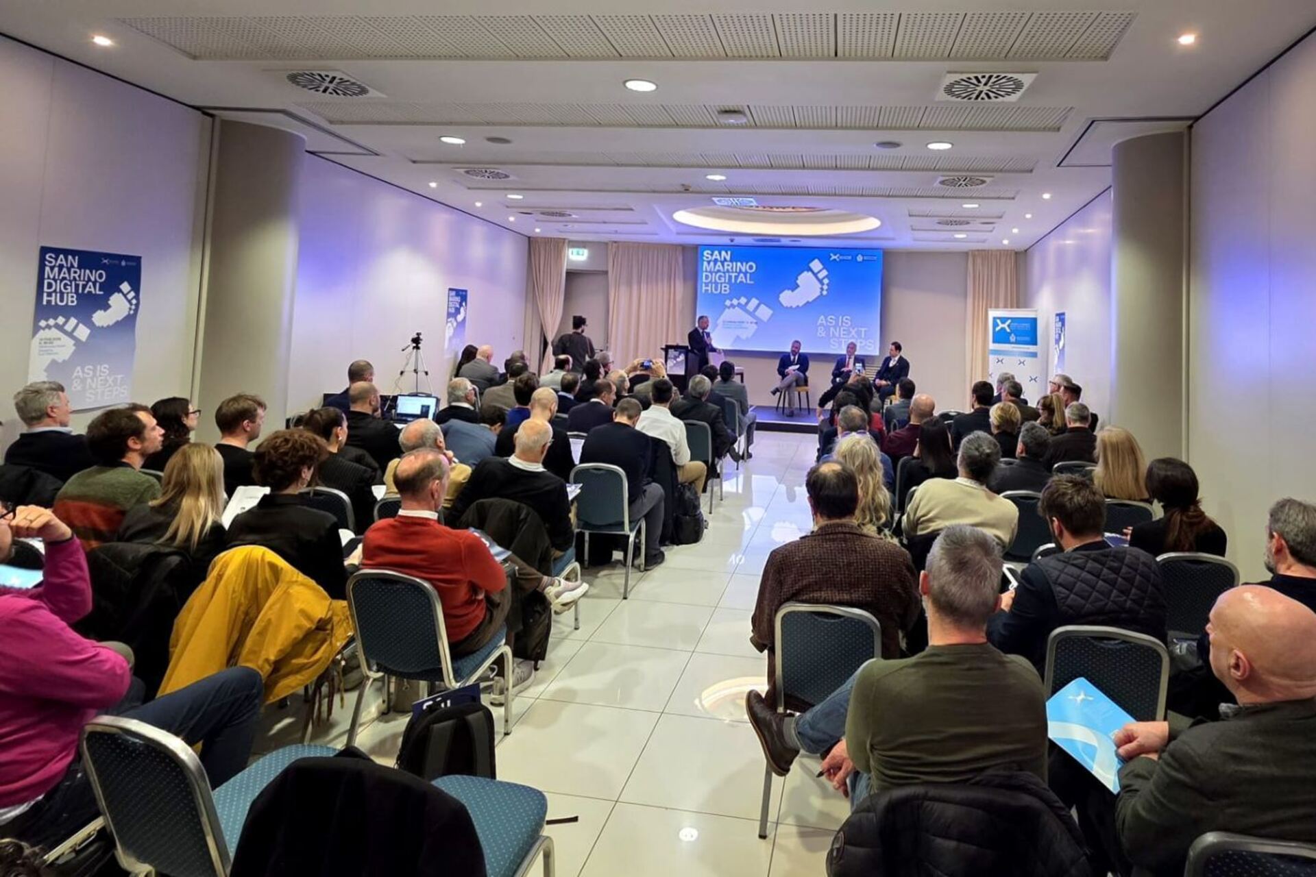 San Marino: conferenza con panel, schermi e materiali informativi dedicati all’ecosistema digitale sammarinese, tra strategie industriali, attrazione di capitali, formazione e innovazione per il futuro