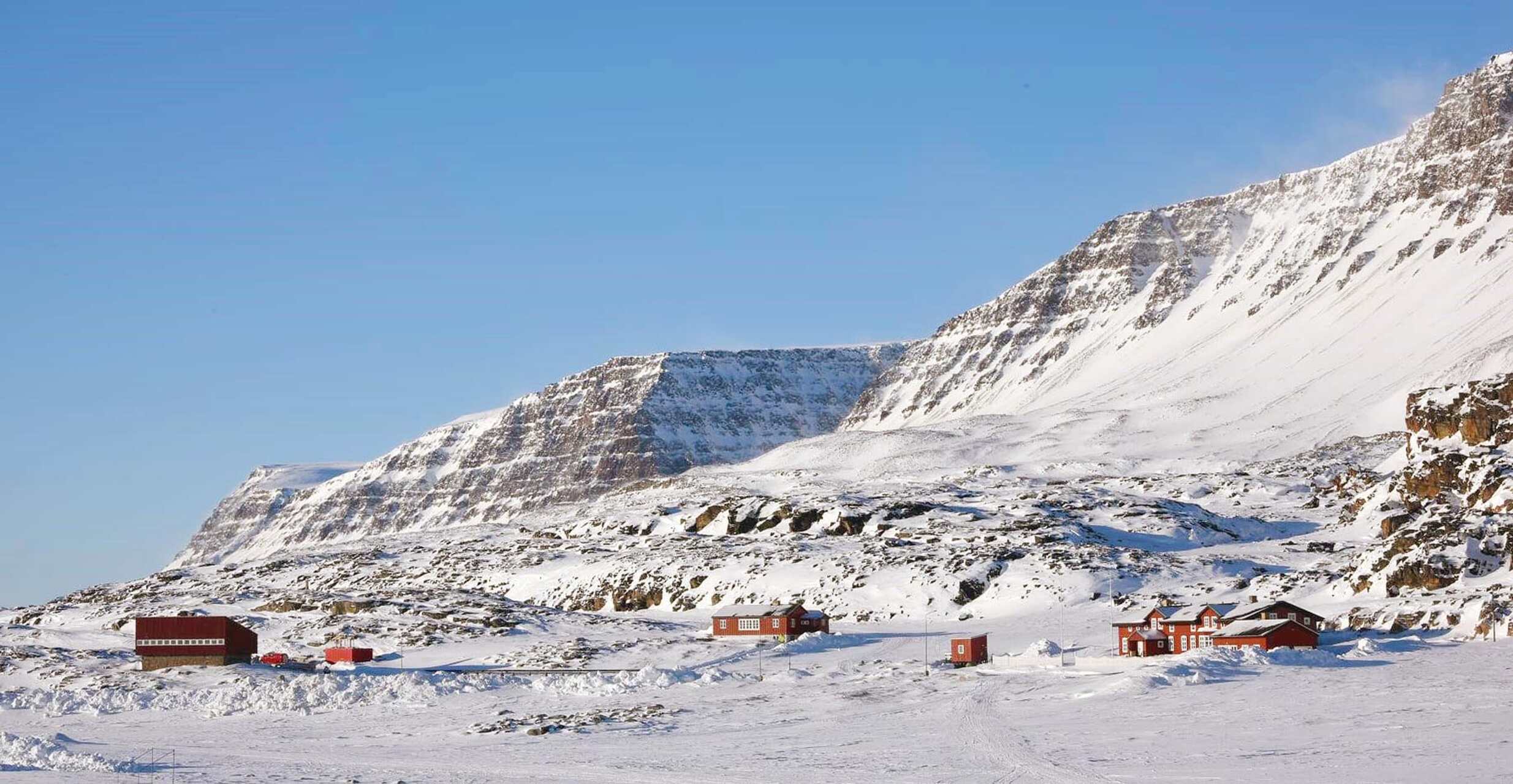 Dansk arktisk station: røde bygninger midt i sne, klipper og bjerge på Diskoøen, i et fjerntliggende landskab hvor klimaforskning og hverdagsliv mødes.