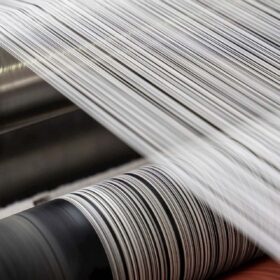 Riciclo tessile: fibre bianche in lavorazione su linee industriali richiamano il passaggio dagli scarti di poliestere a nuovi filati, con processi automatizzati per una moda più circolare