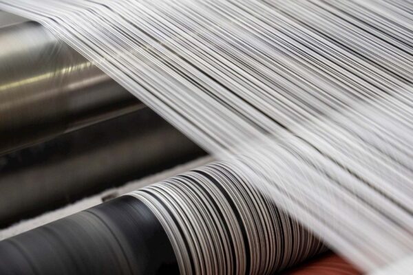 Riciclo tessile: fibre bianche in lavorazione su linee industriali richiamano il passaggio dagli scarti di poliestere a nuovi filati, con processi automatizzati per una moda più circolare